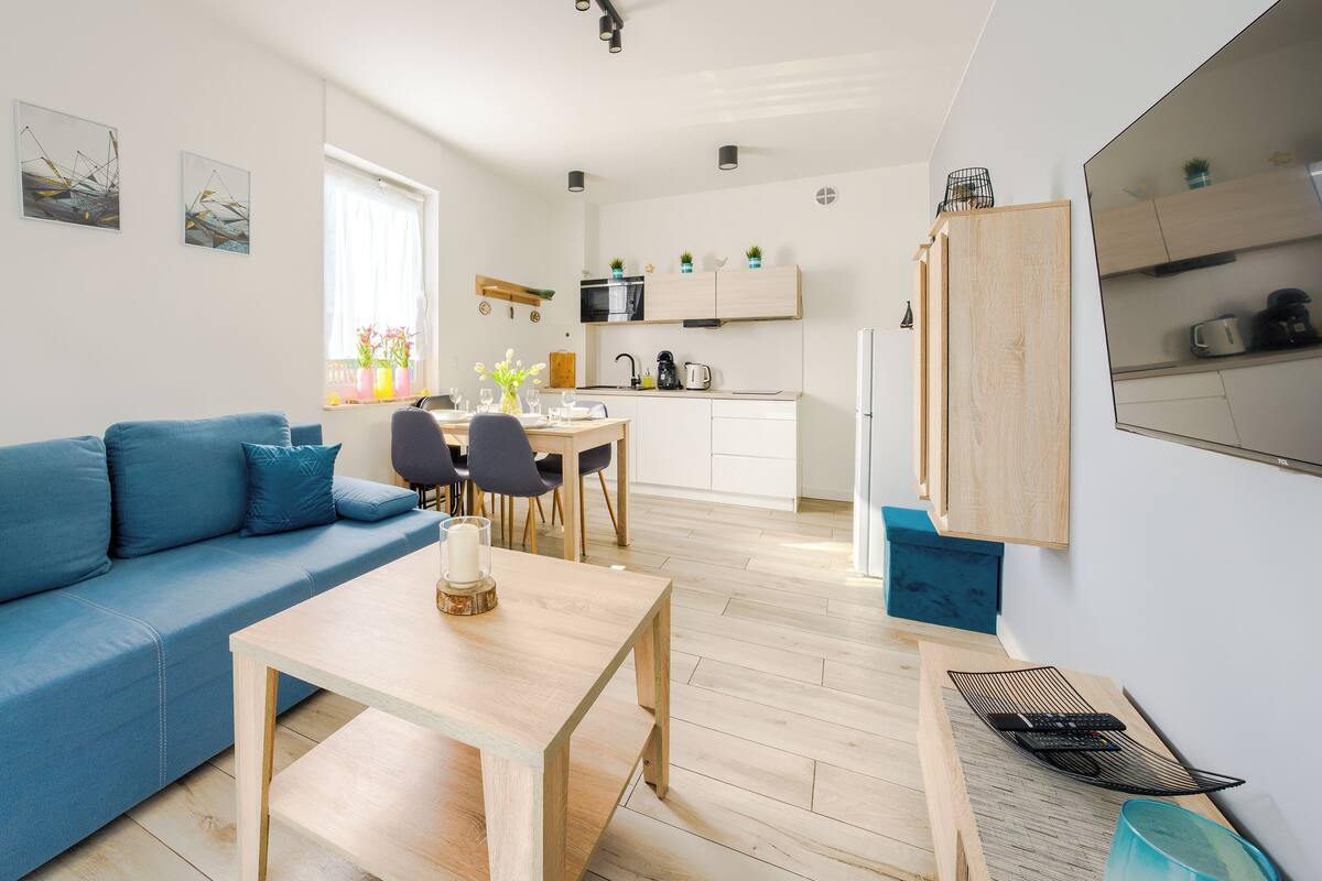 Ein modernes Wohnzimmer mit einem blauen Sofa, einem Holztisch und einem Essbereich mit Stühlen und einem kleinen Tisch.
