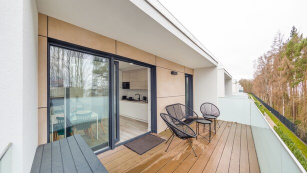 Een modern balkon met een houten terras, glazen deuren naar een keuken en twee zwarte stoelen.