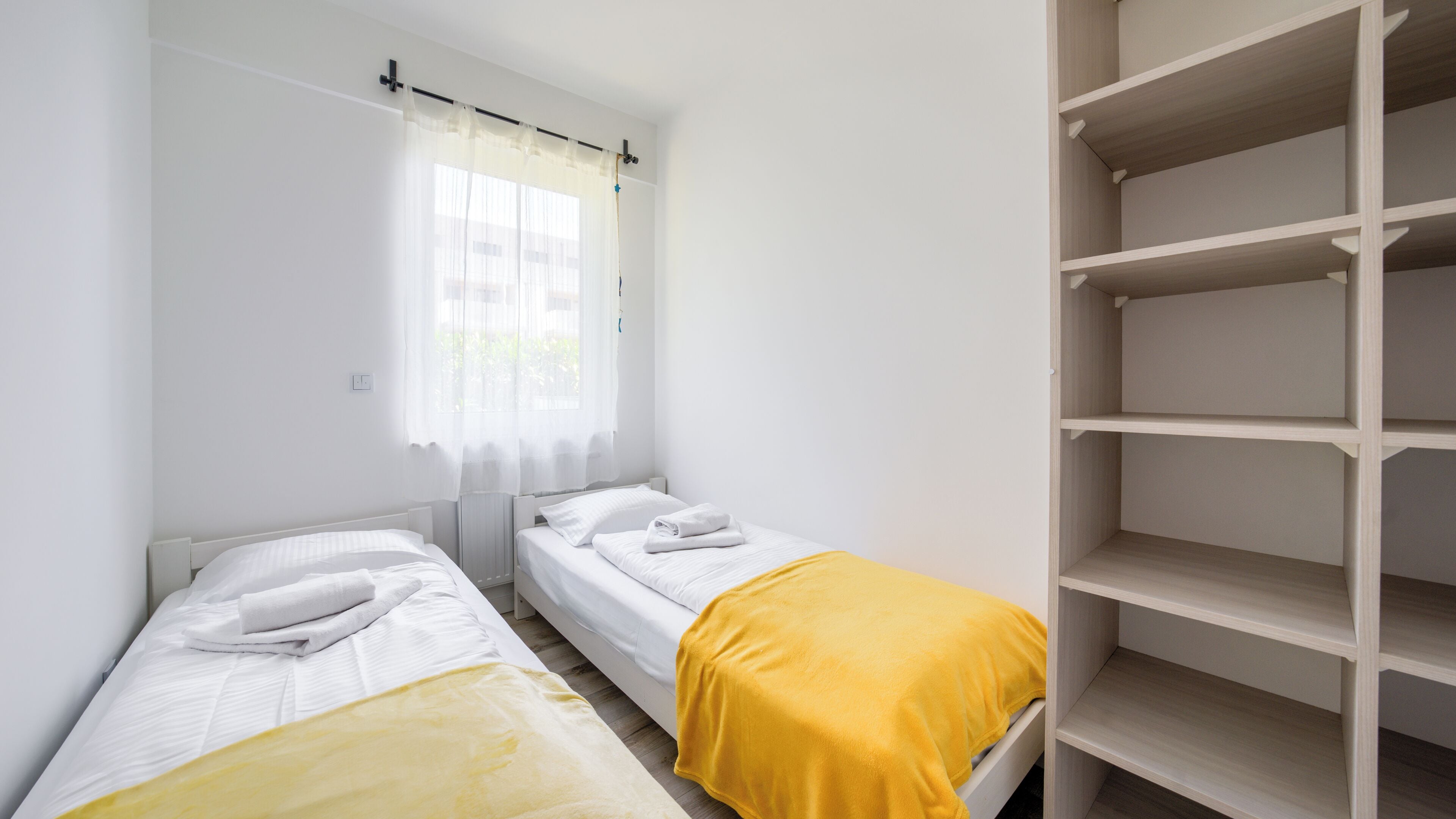 Une chambre avec deux lits simples, une fenêtre avec des rideaux légers et une bibliothèque intégrée.