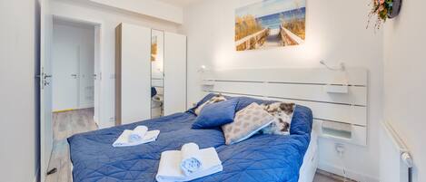 A bedroom with a large bed, a painting of a beach scene, and a white wardrobe.