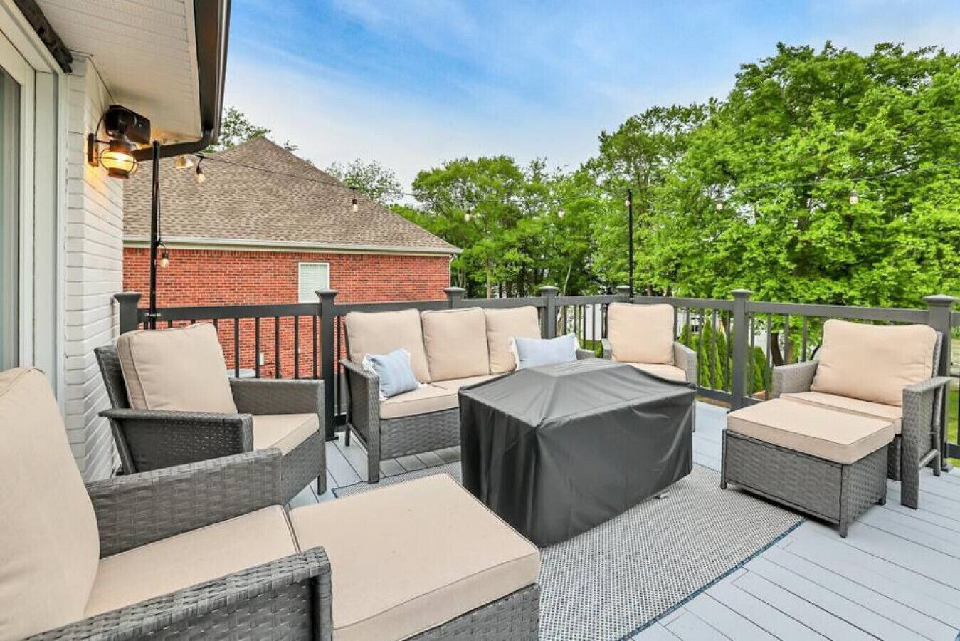 A deck with wicker furniture, including sofas and a table, and a brick building in the background.