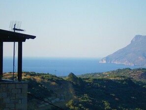 A stone building with a metal roof and an antenna, overlooking a coastal landscape with cliffs and greenery. - Vasiiliki's Residence-Breathtaking View (Kissamos)