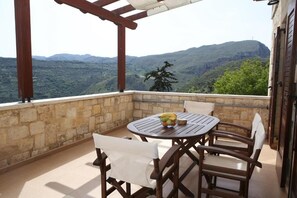 A balcony with a stone wall, wooden chairs, a round table, and a bowl of fruit. - Vasiiliki's Residence-Breathtaking View (Kissamos)