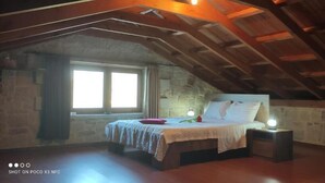 A bedroom with a wooden ceiling, a bed with a white headboard, a nightstand, and a red chair. - Vasiiliki's Residence-Breathtaking View (Kissamos)