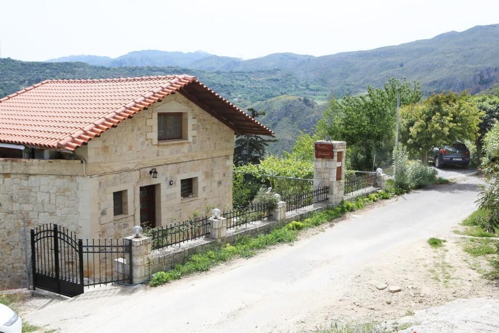 A stone house with a red-tiled roof, a black metal gate, and a dirt road leading to it.