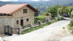 A stone house with a red-tiled roof, a black metal gate, and a dirt road leading to it. - Vasiiliki's Residence-Breathtaking View (Kissamos)