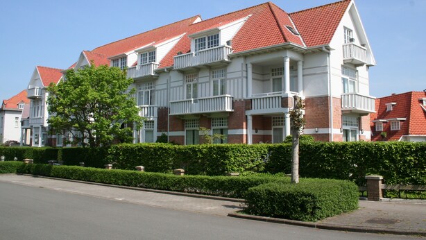 A multi-story residential building with a red-tiled roof, white exterior walls, and multiple balconies.