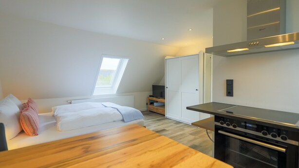 Une chambre moderne avec un lit en bois, une armoire blanche, une télévision et un coin cuisine équipé d’une cuisinière.