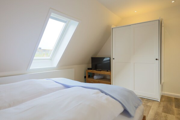 A bedroom with a bed, a TV on a wooden stand, a wardrobe, and a skylight. - Apartment (Westerland)