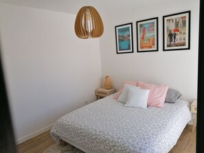 A bedroom with a bed, a hanging light fixture, and three framed pictures on the wall.