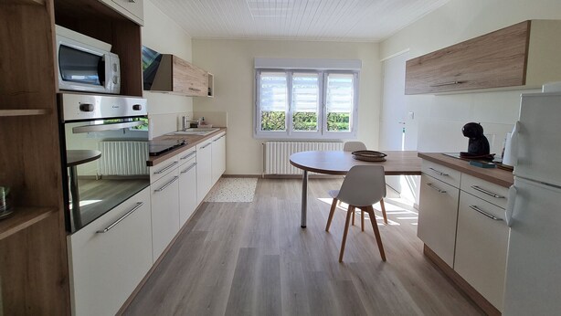 Una cocina moderna con horno empotrado, microondas y refrigerador. Hay una mesa de comedor con sillas y una ventana que proporciona luz natural.