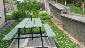 Una mesa de picnic con bancos en un jardín, con un muro de piedra y follaje.