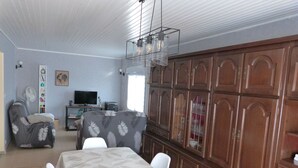 Un comedor con una mesa dispuesta para cuatro personas, un televisor al fondo y un mueble de madera grande.