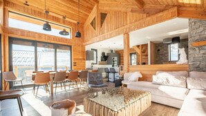 A spacious living area with a wooden ceiling, a glass coffee table, and a stone accent wall. - Luxury chalet for 16 at 150m from cable car in Pra-Loup, sauna, WiFi, non-smoking (Pra-Loup)