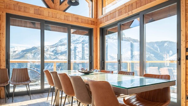 A modern dining area with a glass table and leather chairs, large windows offering mountain views. - Luxury chalet for 16 at 150m from cable car in Pra-Loup, sauna, WiFi, non-smoking (Pra-Loup)
