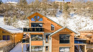 A multi-story wooden cabin with a stone foundation, large windows, and a balcony. - Luxury chalet for 16 at 150m from cable car in Pra-Loup, sauna, WiFi, non-smoking (Pra-Loup)