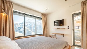 A bedroom with a large bed, a TV mounted on the wall, and a view of mountains through the window. - Luxury chalet for 16 at 150m from cable car in Pra-Loup, sauna, WiFi, non-smoking (Pra-Loup)