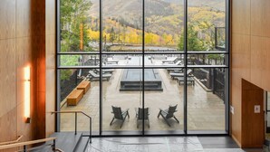 Un interior moderno con ventanas amplias que ofrecen vistas a un patio con mobiliario exterior y un paisaje montañoso.