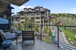 Un balcon avec une chaise et une table, donnant sur un immeuble à plusieurs étages et offrant une vue sur une colline boisée.