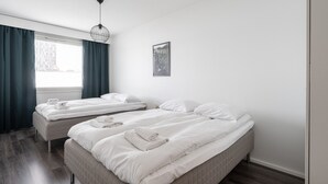 Hotellihuone, jossa on kaksi sänkyä, ikkuna verhoilla, riippuvalaisin ja seinällä oleva kehystetty kuva.