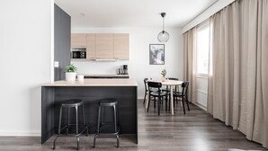 Moderni keittiö, jossa on puiset kaapit, keskellä sijaitseva saareke jakkaroineen sekä ruokailutila pöytineen ja tuoleineen.
