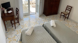 A hotel room with two beds, a desk with a computer, a chair, a wardrobe, and a view of the beach through the sliding glass door. - Hotel Residence Parco Mare Monte (Casamicciola Terme)