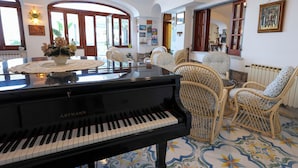 A grand piano in a spacious room with arched windows, wicker chairs, and a tiled floor. - Hotel Residence Parco Mare Monte (Casamicciola Terme)