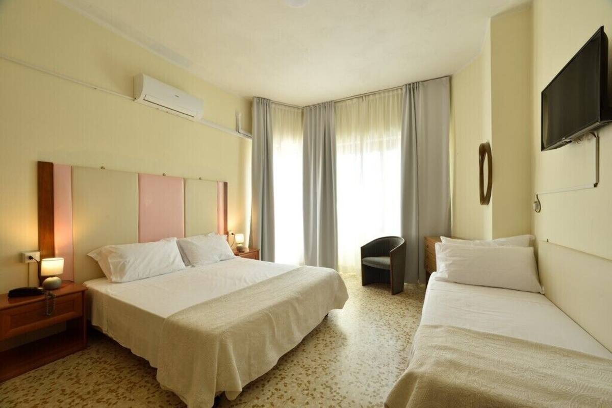 A hotel room with two beds, a flat-screen TV, an air conditioner, and a chair.
