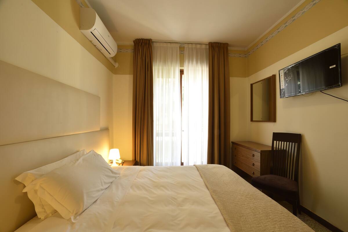 A hotel room with a bed, a dresser, a television, and a window with curtains.