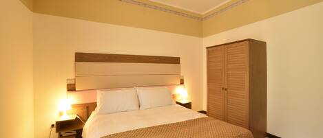 Habitación de hotel con una cama, lámparas de noche, un armario de madera y aire acondicionado instalado en la pared.