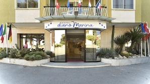 Un hotel llamado "Hotel d'ano Marina" con balcón, banderas y una entrada con alfombra roja.