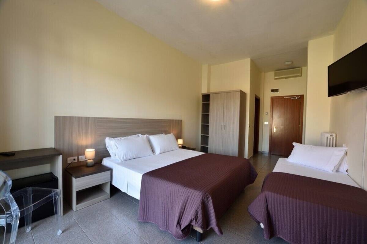 A hotel room with two beds, a desk, a wardrobe, and a TV.