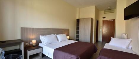 A hotel room with two beds, a desk, a wardrobe, and a TV.