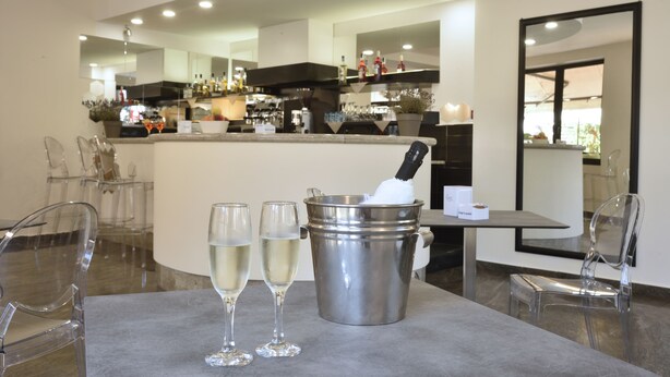 Un moderno comedor con una barra, sillas traslúcidas y una mesa con dos copas de vino blanco y un balde con una botella.