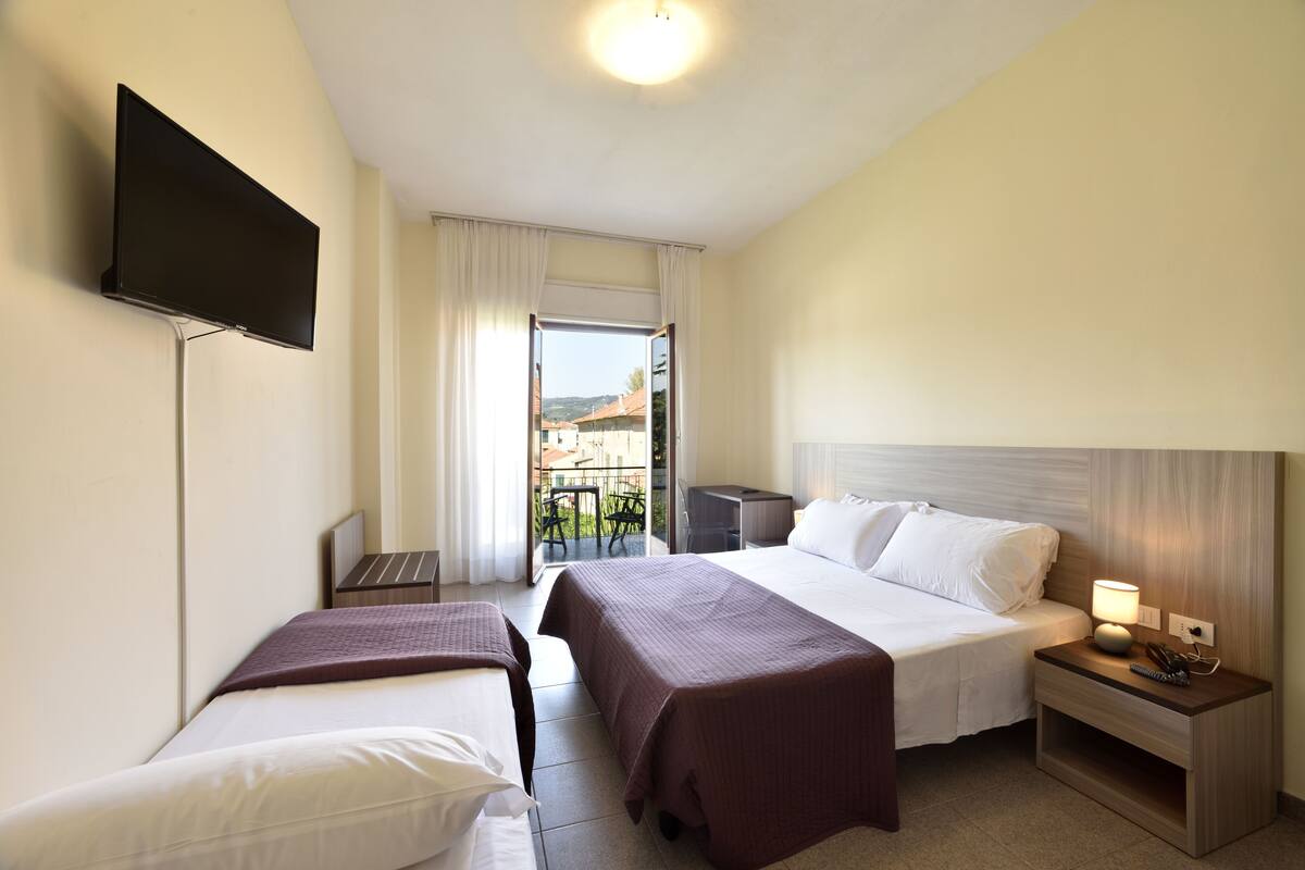 A hotel room with two beds, a TV, a desk, and a balcony with a view.