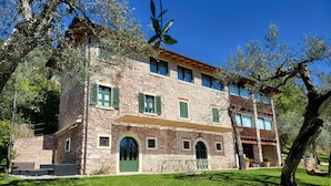 A stone building with a green door and windows, surrounded by trees and grass. - Villa Gran Paradiso (Toscolano-Maderno)