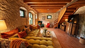 A cozy living room with a stone wall, wooden beams, a sofa, a coffee table, and a fireplace. - Villa Gran Paradiso (Toscolano-Maderno)