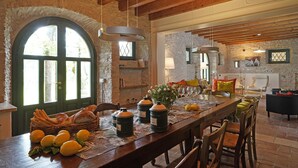 A rustic dining area with a long wooden table, stone walls, and a large arched window. - Villa Gran Paradiso (Toscolano-Maderno)