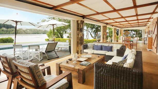 A covered outdoor seating area with a pool view, furnished with wicker chairs and a sofa, and a wooden coffee table. - Villa (Mahebourg)