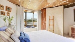 A bedroom with a large bed, a window with a view, a ladder, and a plant. - Villa (Mahebourg)