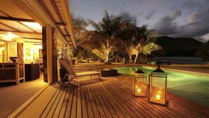 A wooden deck with lounge chairs and a pool, surrounded by tropical vegetation and a mountain backdrop. - Villa (Mahebourg)