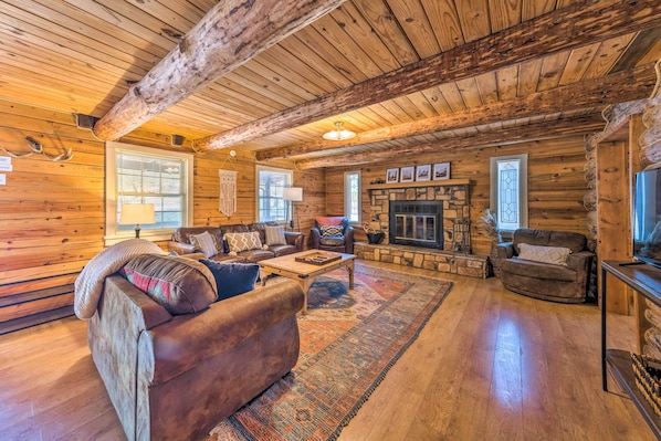 A log cabin interior with a fireplace, wooden walls, and a cozy seating area.
