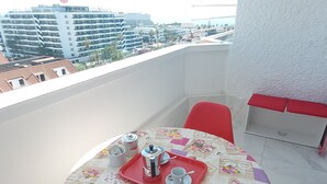 Ein Balkon mit Tisch für zwei Personen, einem roten Stuhl und Blick auf eine Stadtlandschaft mit Gebäuden und Palmen.