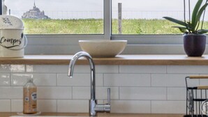 A kitchen with a window view of a field and a distant building.