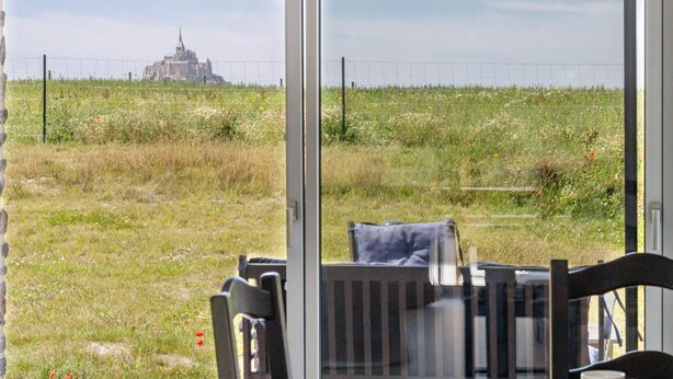 A table with a plate of food and a mug, overlooking a grassy field with a distant building.