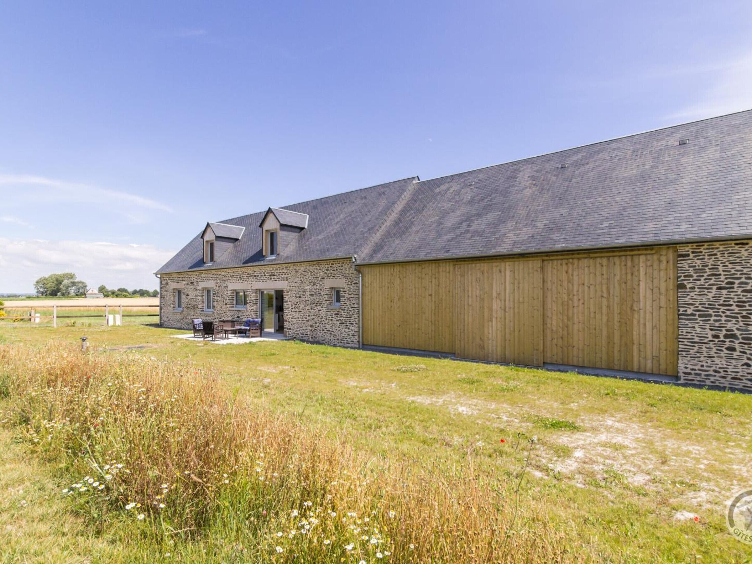 A stone farmhouse with a large wooden barn, a covered outdoor seating area, and a grassy field.