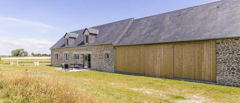 A stone farmhouse with a large wooden barn, a covered outdoor seating area, and a grassy field.
