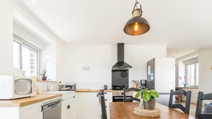 A modern kitchen with white cabinets, a wooden dining table, and a hanging light fixture.