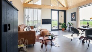 En rummelig opholdsstue med højt til loftet, en lædersofa, et spisebord og et stort vindue med udsigt til det fri.
