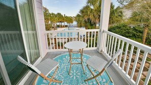 A balcony with a round table and two chairs, overlooking a pool and palm trees.